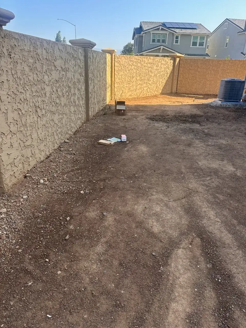New-build backyard before landscaping: bare soil and stucco walls