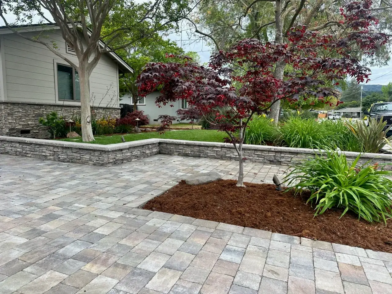 Block retaining wall and Japanese maple beside a paver driveway.