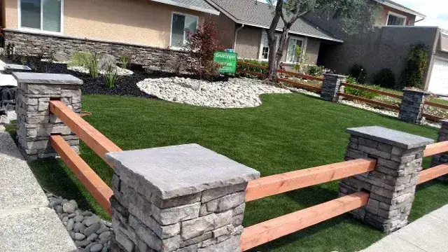 Artificial turf front yard with stone pillars and a redwood rail fence