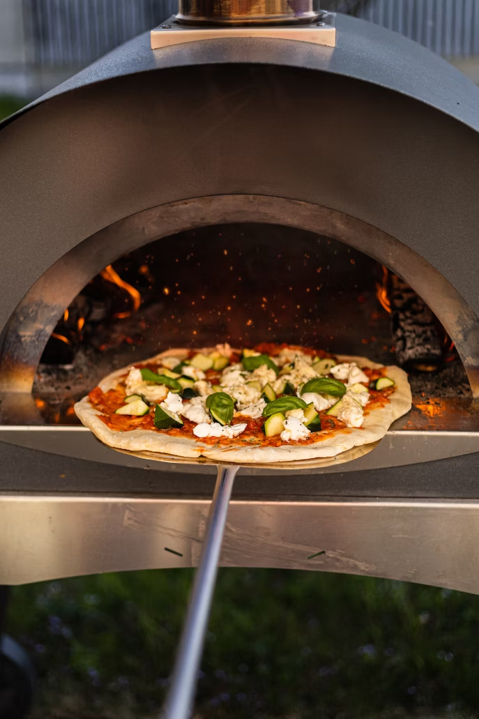 A person cooks in an outdoor pizza oven.
