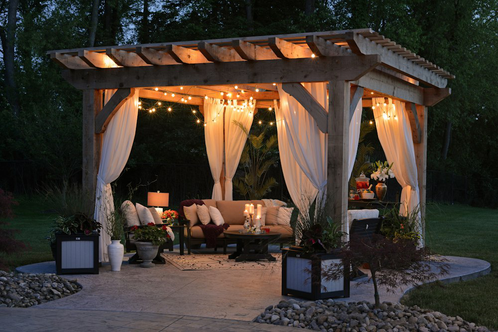 Cozy outdoor living space with concrete patio and wooden pergola adorned with lights and curtains, demonstrating concrete’s versatility in garden design.
