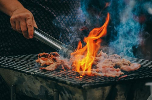 Man grilling meat in an outdoor kitchen with a landscaped backyard featuring hardscaping and greenery.