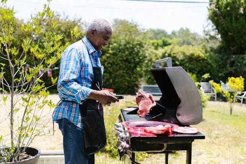Man-cooking-out-side Man cooking outside in an outdoor kitchen with integrated hardscaping, lighting, and natural landscaping.
