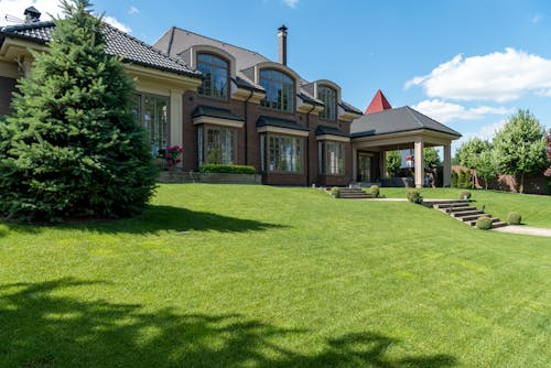 View of a mansion with stunning landscape renovation, featuring artificial turf installation and elegant hardscape design.