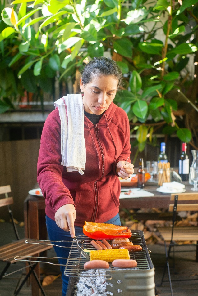 Woman-grilling-in-an-outdoor-kitchen Woman using a grill in an outdoor kitchen surrounded by professionally landscaped elements and greenery.